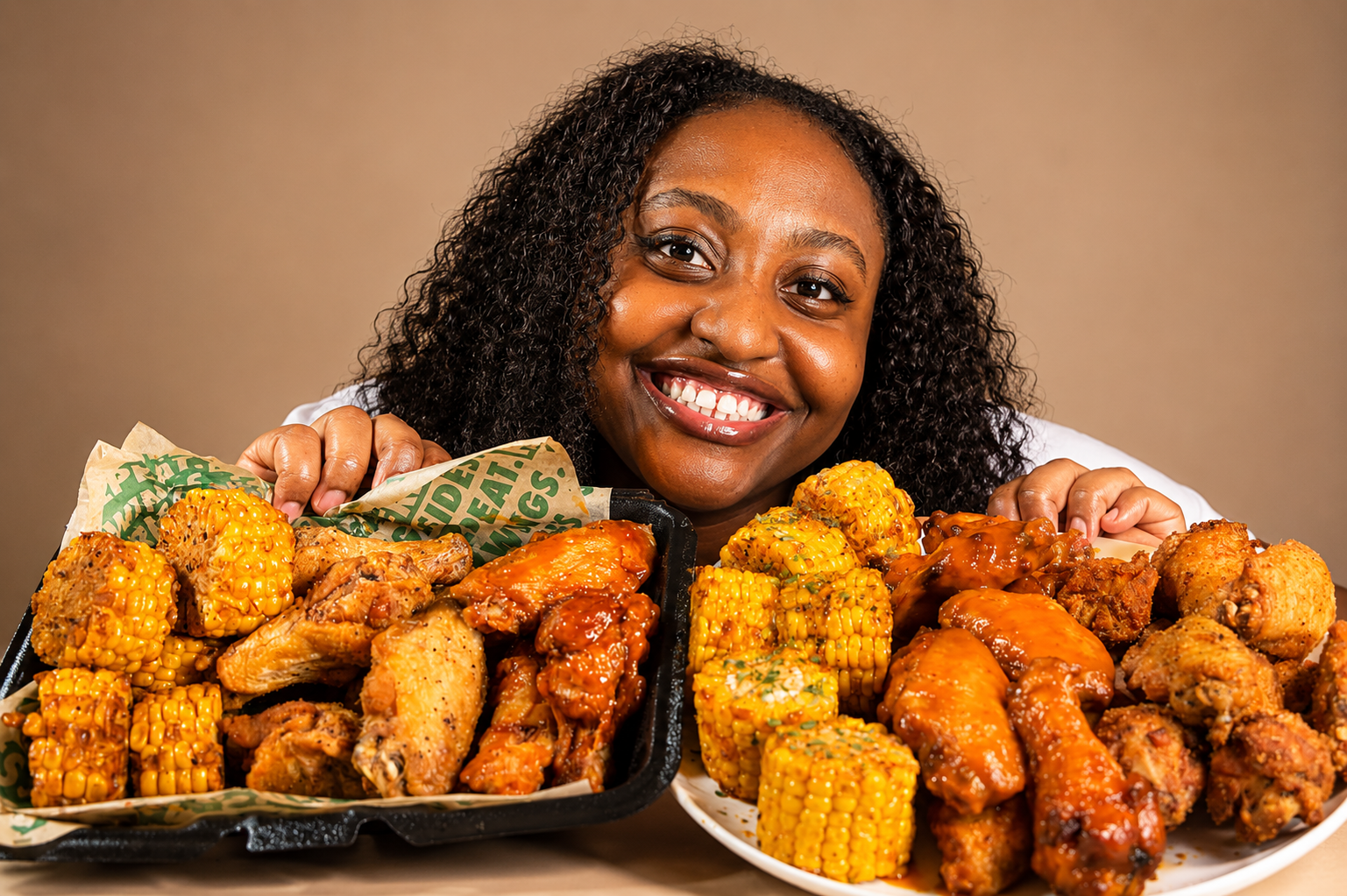 Jess smiling behind a large platter of fried chicken wings and corn on the cob